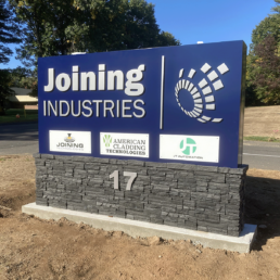 Blue sign on stone base for American Cladding Technologies, a Joining Industries company.